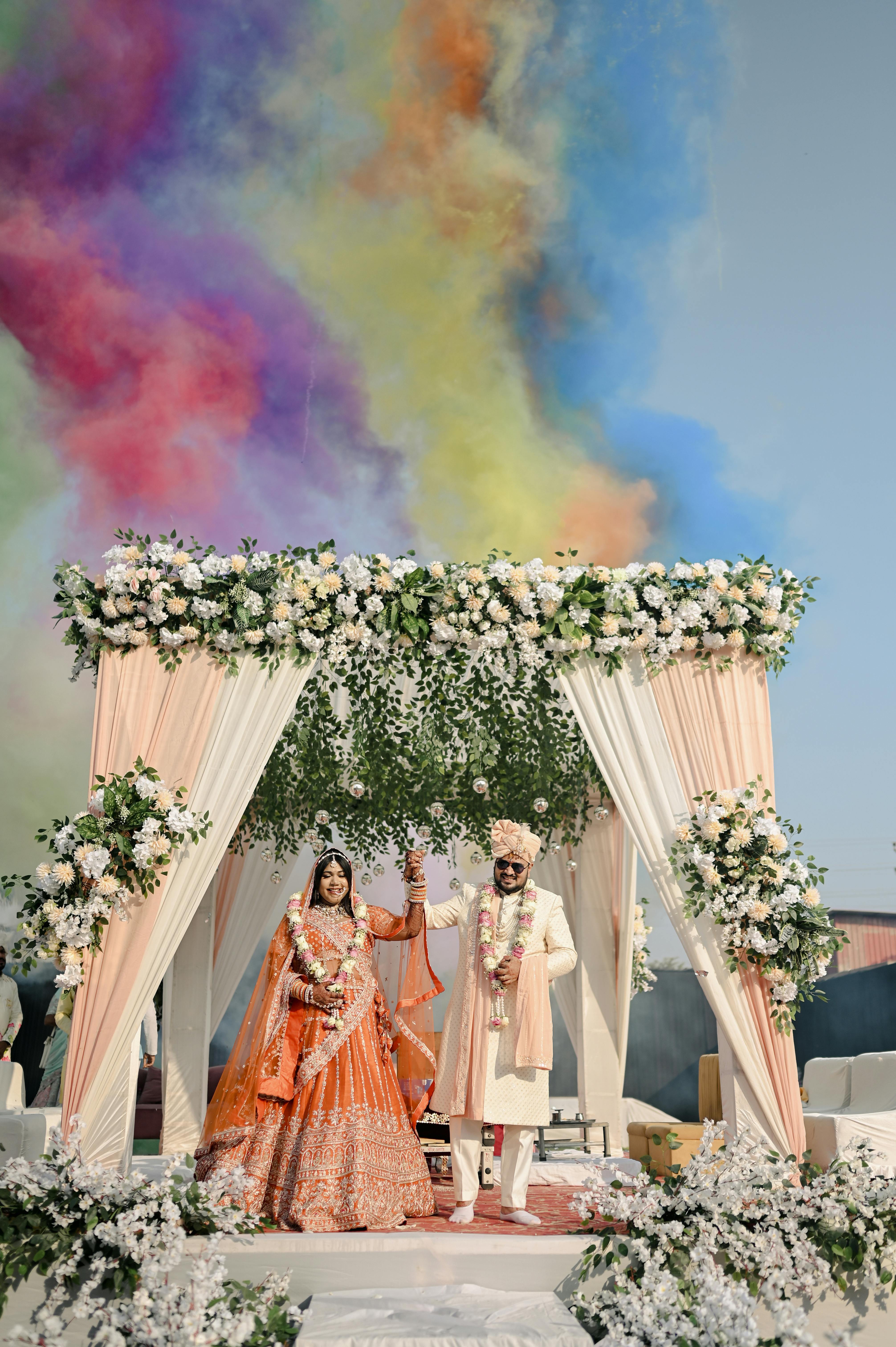 Colorful outdoor wedding ceremony with floral mandap and joyful couple.